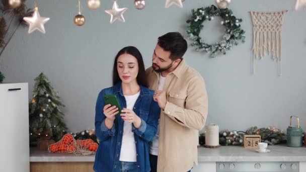 恋愛のカップルは モダンな居心地の良いオルネイトキッチンで冬のクリスマスの新年の休日を楽しんで携帯電話を持っています 現代の技術の使用法 オンラインで自由な時間を過ごし インターネットで楽しみ Xmas Eveの概念の新しいアプリを使用して下さい — ストック動画