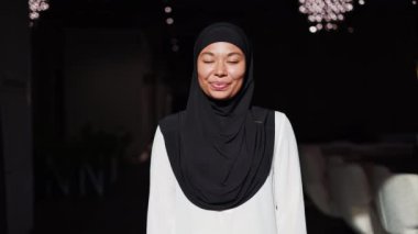 Siyah tesettürlü güzel Afro-Amerikan kadın modern ofiste kollarını kavuşturarak poz veriyor. Başarılı bir iş kadını. Yüzünde samimi bir gülümseme var. İş yerinde kameraya bakıyor..