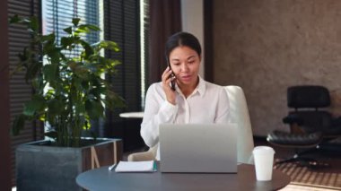 Dost canlısı bayan yönetici portatif dizüstü bilgisayarın önünde oturuyor ekrana bakıyor ve cep telefonuyla konuşuyor. Beyaz bluzlu Afro-Amerikalı olgun kadın modern ofiste uzaktan pazarlık yapıyor..