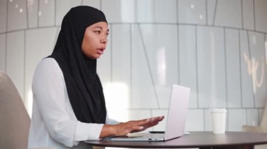 Siyah tesettürlü endişeli çok kültürlü kadın kablosuz bilgisayarla çalışırken açıklanamaz bir korku ve el titremesi yaşıyor. Modern kurumsal çalışma alanında panik atak geçiren olgun bir bayan..