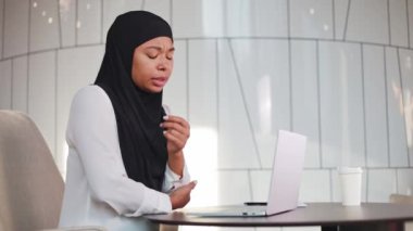 Siyahi tesettürlü çok ırklı kadın modern ofisteki sabit çalışma yüzünden dirsek ağrısından muzdarip. Hüzünlü kadın yönetici, kablosuz bilgisayarla masada oturuyor ve ofis sendromlu el ağrısı çekiyor..