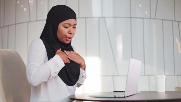 職場に座りながら痛みや呼吸をコントロールするために胸をマッサージする多文化女性 無線ラップトップでストレスの多い仕事の後に健康に問題を抱えているヒジャーブの女性 — ストック動画