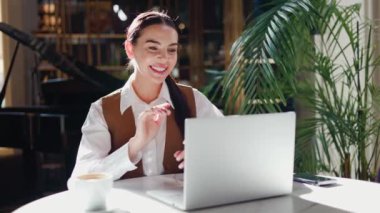 Bir kafedeki kadın bir dizüstü bilgisayar video görüşmesine katılıyor, uzaktan çalışıyor, çevrimiçi toplantı düzenliyor ya da sanal danışmanlık yapıyor. Samimi bir ortamda profesyonel iletişimin kusursuz bir karışımı..