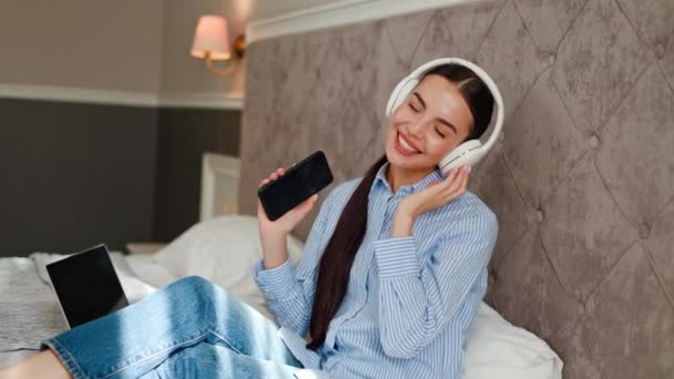 Oszałamiająca Dziewczyna Siedzi Łóżku Hotelu Trzymając Telefon Komórkowy Tańcząc Słuchając — Wideo stockowe
