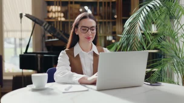身着西装的自由女作家坐在一家正在笔记本电脑上工作的餐厅里 女经理拿起一杯卡布奇诺和饮料 做与公司收入和支出有关的远程工作的女士 — 图库视频影像