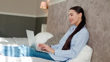 Yatak odasında duran sevimli kadın gülümseyerek kameraya bak, arkadaşını selamla, otel odasındaki video çağrısına katıl. Kadın sanal buluşma olayı, iletişim mesafesi dizüstü bilgisayar kullanımı. Görüntülü konuşma.