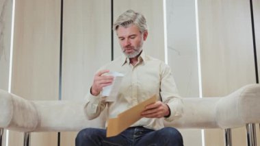 Mutsuz, beyaz saçlı, elinde mektupla kanepede oturan beyaz bir adam. Resmi giyinmiş yaşlı bir girişimci iş yerindeki kötü haberlerden büyük hayal kırıklığı yaşıyor..