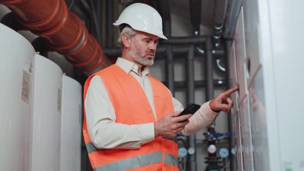 有经验的工厂工人穿着橙色安全背心 而不是白衬衫 在高科技设备上执行任务 在现代智能手机的帮助下 戴着白盔的资深男性数据集中在一起 — 图库视频影像