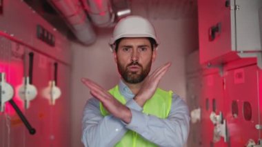 Koruyucu yelek giyen elektrik mühendisi ve kollarını kavuşturan beyaz miğfer tehlike sinyali veriyor. Trafo çalışanı, yüksek voltaj ve hatalı elektrik donanımından dolayı kırmızı ışıkta durmamızı söylüyor..