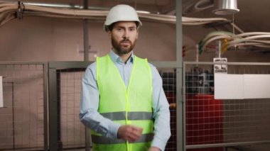 Profesyonel erkek mühendis elektrik santralinin teknik odasında duruyor, yeşil güvenlik yeleği giyiyor, elektrik santrali ortamında güvenlik başlığı takıyor..