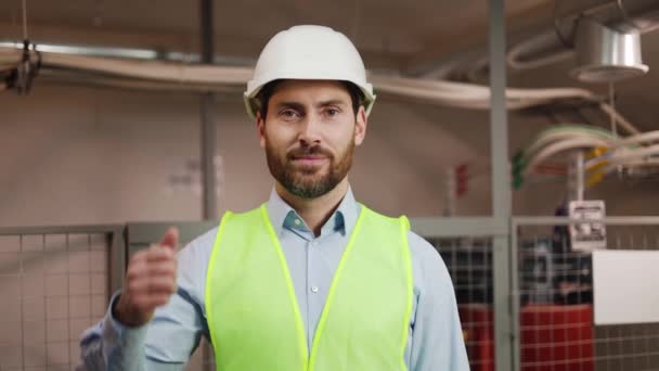 冶金车间的工人戴着白色的头盔和背心 站在电源开关房中竖起大拇指 工程师技师对着摄像机笑 协调行动 — 图库视频影像