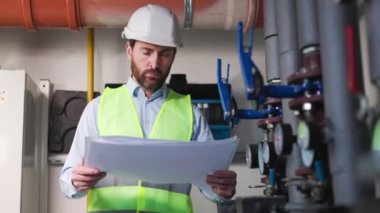 Fabrikada inşaat planı üzerinde çalışan deneyimli bir tesisatçı. Ciddi işçi belgeleri okuyarak projeyi analiz ediyor ve ısıtma için yapay zekaya sahip programlar yerleştirmeyi düşünüyor..