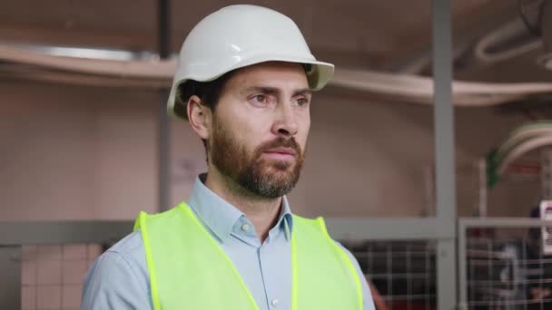外型男工程师站在电气总机的技术室 身穿绿色安全背心 在变电站环境中戴安全帽 专业工程 — 图库视频影像