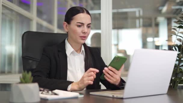 Mulher Negócios Séria Trabalhando Com Laptop Moderno Segurando Smartphone Mão — Vídeo de Stock