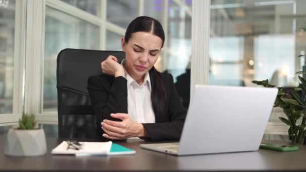 デジタルコンピュータの前に座り 肘の屋内で重い痛みを感じている暗い髪の不満の女性マネージャー オフィスの鎮静剤の仕事の後で手をマッサージするUpsetの慎重な起業家 — ストック動画