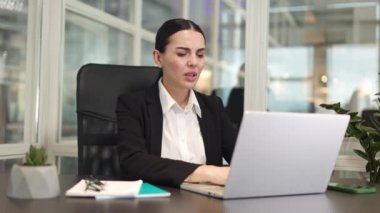 Modern ofiste oturan hasta bir iş kadını ağır karın ağrısı çekerken kablosuz bilgisayar kullanıyor. Beyaz tenli esmer, parlak bir binada çalışıp acıdan kıvranıyor..