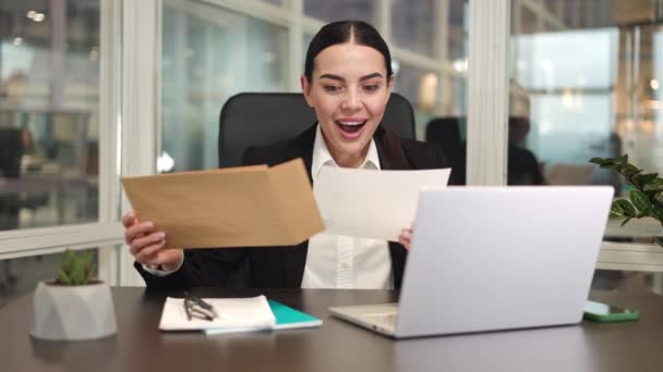陽気な女性起業家が座って近代的なガジェットを使用しながら 封筒から素晴らしいニュースで手紙を取り出します 満足した慎重なマネージャーがオフィスの昇進の内容でシートを得る — ストック動画