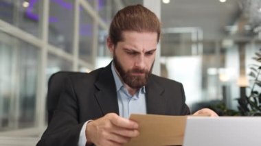 Gergin, genç, beyaz bir erkek, ofisinde modern bir dizüstü bilgisayarla masada otururken elinde kağıt bir mektup tutuyor. Memnuniyetsiz işadamı belgeyi açmaya ve önemli bilgileri içeride okumaya hazırlanıyor..