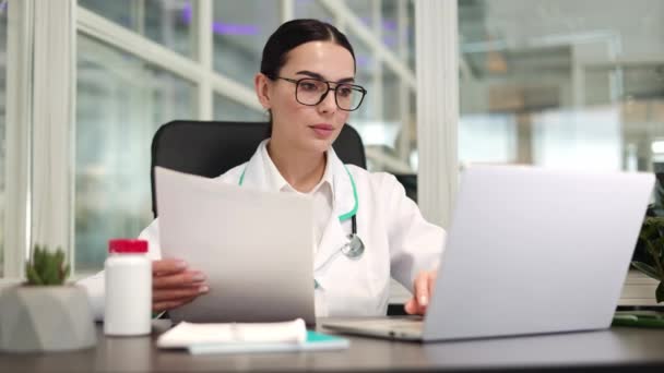 Médica Focada Sentada Mesa Trabalhando Com Dispositivo Digital Segurando Documentos — Vídeo de Stock