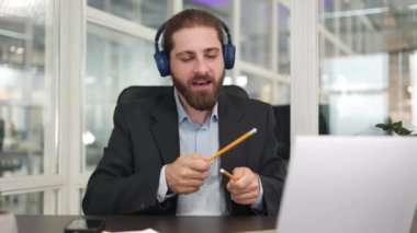 Ofisin içinde taşınabilir dizüstü bilgisayar üzerinde çalışırken resmi giysiler içinde eğlenen genç Kafkasyalı Kafkasyalı. Neşeli adam kalemi baget olarak kullanıyor ve evde sanal davul çalıyor..