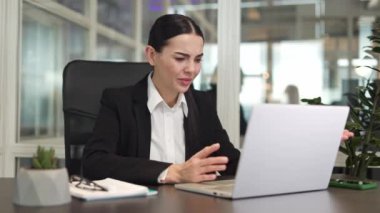 Gergin kadın girişimci, koyu renk ceketiyle ofiste el ele otururken modern dizüstü bilgisayarda çalışmakta güçlük çekiyor. İş yerinde sorunlar ve başarısızlıklar kavramı.