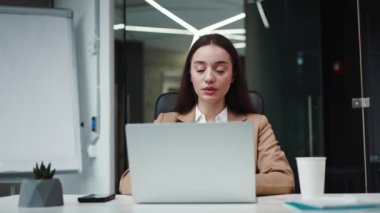 Kafkasyalı beyaz bir iş kadınının portresi modern dizüstü bilgisayarın önünde oturuyor ve düşünüyor. Zarif takım elbiseli bayan ofis çalışanı hafif bir gülümsemeyle başka tarafa bakıyor. Teknoloji kavramı.