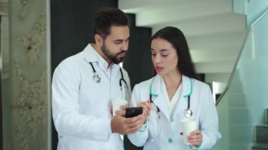 Elinde kahve tutan çekici bir kadın ve hastane koridorunda ayakta dururken elinde modern akıllı telefon tutan yakışıklı sakallı adama bir şey anlatıyor. Kahve molası veren iki uzman doktor..