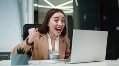 Taşınabilir laptop kullanan harika bir iş kadını ve iyi bir kariyer haberi karşısında şokta. Şık bir ofis elbisesi içinde heyecanlı bir kadın yumruğunu sıkar ve samimi mutluluğunu ifade eder..