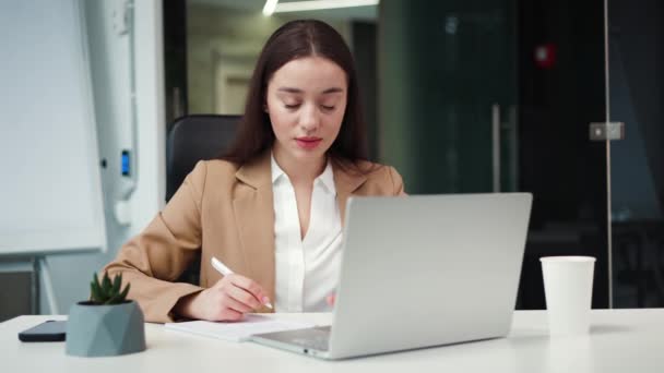 在当代办公室里 穿着时髦西服的迷人的黑发女士坐在无线笔记本电脑旁 成功的高加索经理在舒适的橱柜里填写申请表和解决工作细节 — 图库视频影像