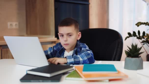 可爱的高加索男孩坐在舒适的室内椅子上 在现代笔记本电脑上打字 在家教期间 聪明的孩子在网上平台上看着相机做作业 — 图库视频影像