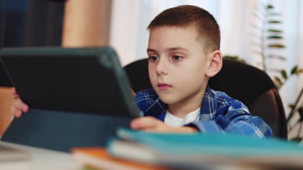 白人男性の子供は 宿題をするために黒いケースでデジタルタブレットを使用してカジュアルな服を着ていました 現代のガジェットを使用して電子学習で責任を持って行動する集中した表現を持つ子供 — ストック動画