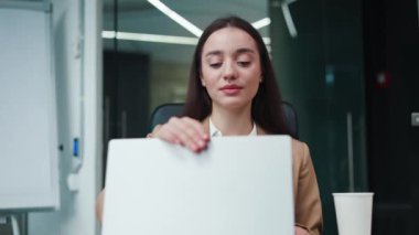 Gülümseyen beyaz kadın kablosuz bilgisayarı yavaşça açıyor ve iş yapmaya hazırlanıyor. Koyu renk saçlı, beyaz bir kadın profesyonel çalışma alanında ofis çalışanı olarak kariyer yapıyor..