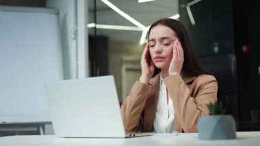 Ofis masasında kablosuz bilgisayarla oturan ve acıdan suratını buruşturan siyah saçlı, yorgun bir kadın yönetici. İş elbisesi giyen genç bayan çalışma sırasında şiddetli migren ağrısı çekiyor..