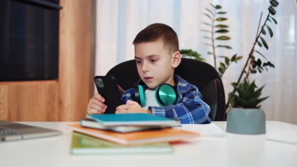 Keskittynyt Koulupoika Pukeutunut Tarkistettuun Paitaan Istuu Pöydässä Katselee Videoita Älypuhelimella — kuvapankkivideo