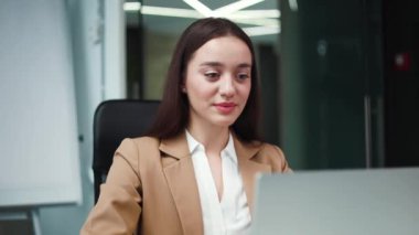 Resmi takım elbiseli, gülümseyen beyaz iş kadını profesyonel iş yerinde olumlu jest yapıyor. Neşeli kadın ifadesi mutluluk ve baş parmakla mutabakat göstergesi.