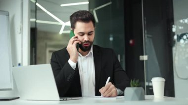 Çağdaş ofiste otururken, kendine güvenen, resmi giyinmiş sakallı bir adam cep telefonunu arama için kullanıyor. Erkek işveren çalışma detaylarını tartışmak için partnerle randevu ayarlıyor.