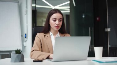 Çekici esmer kadın iş yerinde portatif bilgisayarla yan yana otururken yan bakıyor. Kurumsal ofiste yeni iş fırsatları düşleyen kendine güvenen beyaz bir iş kadını..