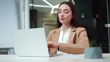 Yorgun, beyaz bir kadın ofis içi bilgisayarında yoğun çalışma sırasında yorgun vücudunu esnetiyor. Resmi olarak çalışkan bir kadın iş yerinden kalkmadan ısınıyor..