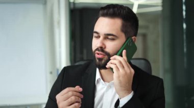 Yakışıklı beyaz adam iş arkadaşıyla modern akıllı telefondan ciddi ciddi konuşuyor. Şık bir iş elbisesi giymiş konsantre bir erkek ofis merkezindeki müfettişe sakince fikrini açıklıyor..