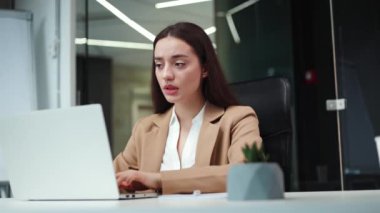 Koyu renk saçlı üzgün iş kadını modern dizüstü bilgisayarda yazı yazıyor ve iş yerinde aniden diş ağrısı çekiyor. Beyaz kadın çalışan, parlak bir şirket ofisinde acı çekerken yanak yanağa duruyor..