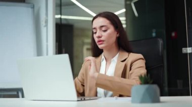 Hüsrana uğramış iş kadını ofis masasında oturup modern dizüstü bilgisayarda yazarken boynundaki acıyı hissediyor. Koyu saçlı, üzgün, beyaz bir kadın uzun süreli çalışma sırasında kas gerilimi yüzünden stres altında..