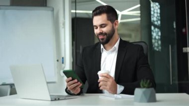 Sakin bir erkek iş arkadaşlarıyla telefonda mesajlaşıyor ve iş yerinde kahve içiyor. Gülümseyen beyaz iş adamı önemli insanlarla iletişim kurmak için teknolojiyi kullanıyor. İletişim kavramı.