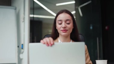 Kafkasyalı güzel bir kadının portresi geniş tasarımcı dolabının arka planında kablosuz modern bilgisayarı kapatıyor. Neşeli esmer kadın ofis içi iş planını tamamlıyor..