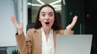 Neşeli beyaz kadın vay canına diye bağırıyor çünkü kişisel laptopta olumlu haberler görüyorum. Mutlu iş kadını modern aletlerle çalışıyor ve sonuçtan zevk alıyor. Başarı ve teknoloji kavramı.