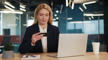 Resmi takım elbiseli bir iş kadını kablosuz bilgisayarla çalışıyor ve elinde banka kartı tutuyor. Ofiste sipariş veriyor. Kafkas tebessüm müdürü modern aletlerle başarılı internet alımına seviniyor..