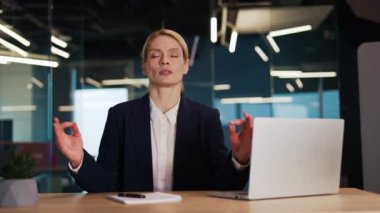 Mudra el hareketleriyle katlanmış bir şekilde işyerinde oturan, iş günlerinde stresi azaltan, meditasyon yapan ya da ofiste yoga yapan genç kadın işkadını..