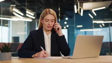 Ofisindeki bilgisayarın başında oturan güzel bayan ofis müdürü telefonda konuşuyor. Güzel bir iş kadını cep telefonuyla konuşuyor ve bilgisayarla çalışıyor..