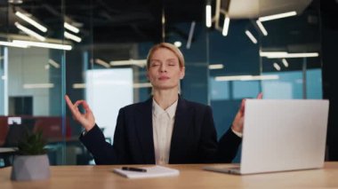 Yorgun iş kadını işini dizüstü bilgisayarla bitir ve Mudra hareketi yaparken sandalyenin arkasına yaslan. Resmi takım elbiseli konsantre bir kadın mola veriyor ve kişisel iş yerinde meditasyon yapıyor..
