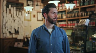 Lokanta ortamında kollarını kavuşturmuş neşeli, sakallı, kendine güvenen bir asilzade. Tişört ve siyah önlük giymiş pozitif garson iyi hizmet vereceğine dair güvenini dile getiriyor..