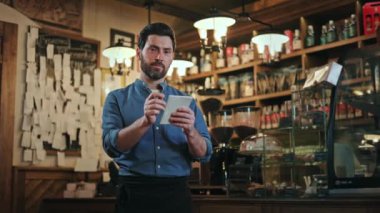 Üniformalı, arkadaş canlısı sakallı bir adamın portresi. Kaliteli bir barda dikilirken kağıda sipariş yazıyor. Çalışırken gülümseyen ve kameraya bakan becerikli erkek garson..